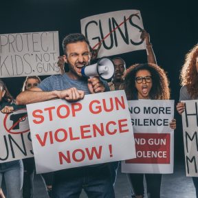 angry man holding placard with stop gun violence now lettering and screaming in megaphone near